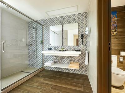 Modernes Badezimmer mit Holzfußboden, Glasscheibendusche und zwei Waschbecken an einer gemusterten Wand.