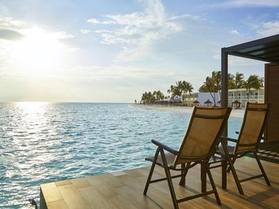 Zwei Liegestühle auf einer Terrasse mit Blick auf das Meer und Palmen bei Sonnenuntergang.