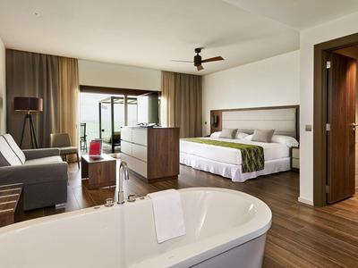 Modern eingerichtetes Hotelzimmer mit freistehender Badewanne, Bett, Sofa und Balkon.