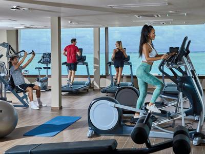 Persone che si allenano in una palestra moderna con grandi finestre che si affacciano sul mare.