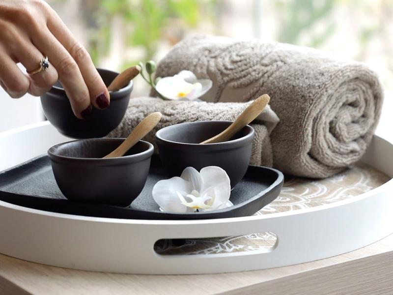 Ein Tablett mit zwei Schalen, Holzlöffeln und einem zusammengerollten Handtuch neben weißen Blüten.