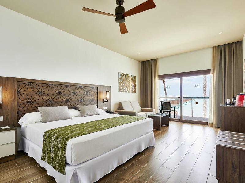 Helles Hotelzimmer mit großem Bett, Holzboden und Balkon mit Meerblick.