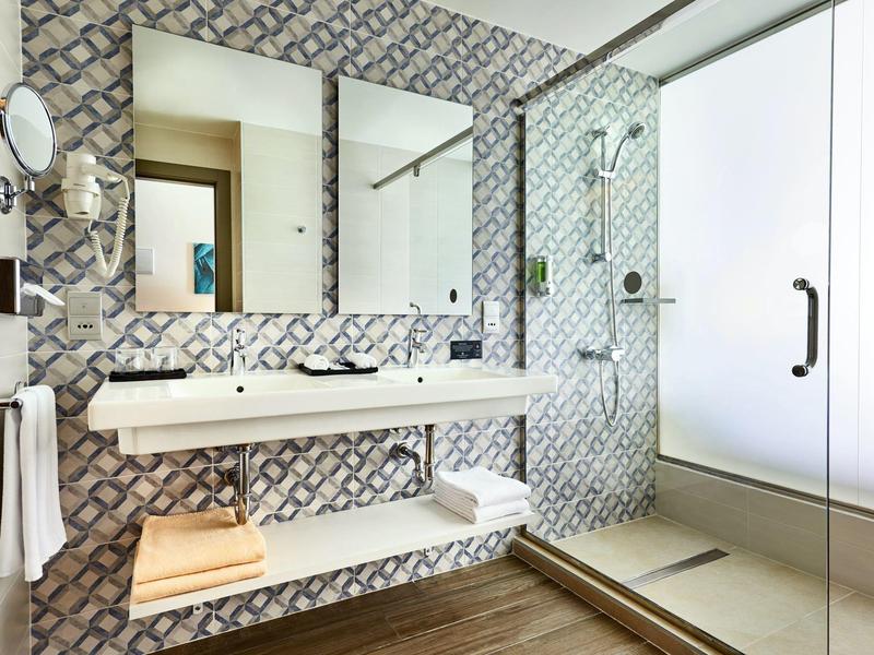 Modernes Badezimmer mit doppeltem Waschbecken, Glasdusche und dekorativen Wandfliesen.