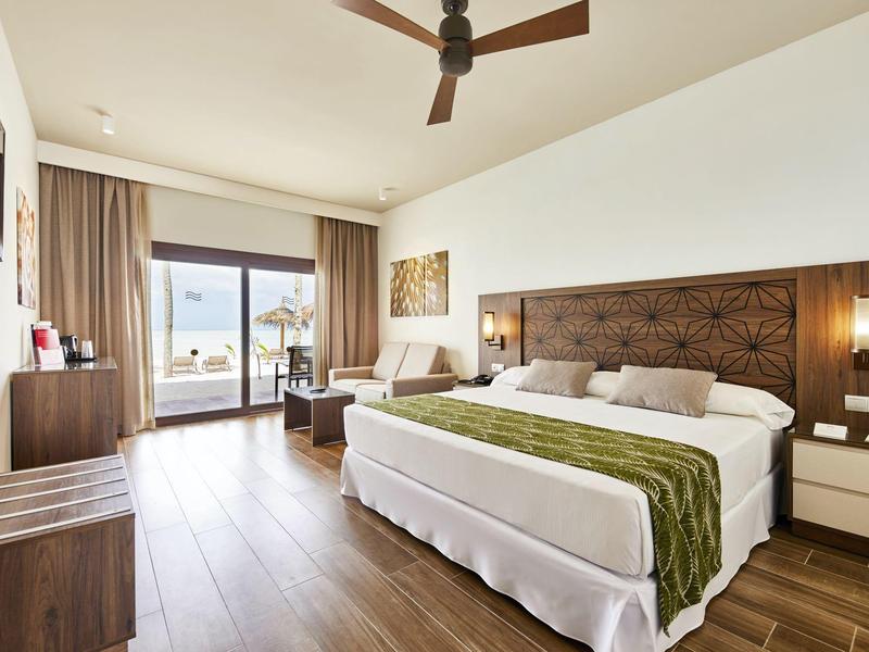 Modernes Hotelzimmer mit großem Bett, Holzboden und Blick auf Balkon und Meer