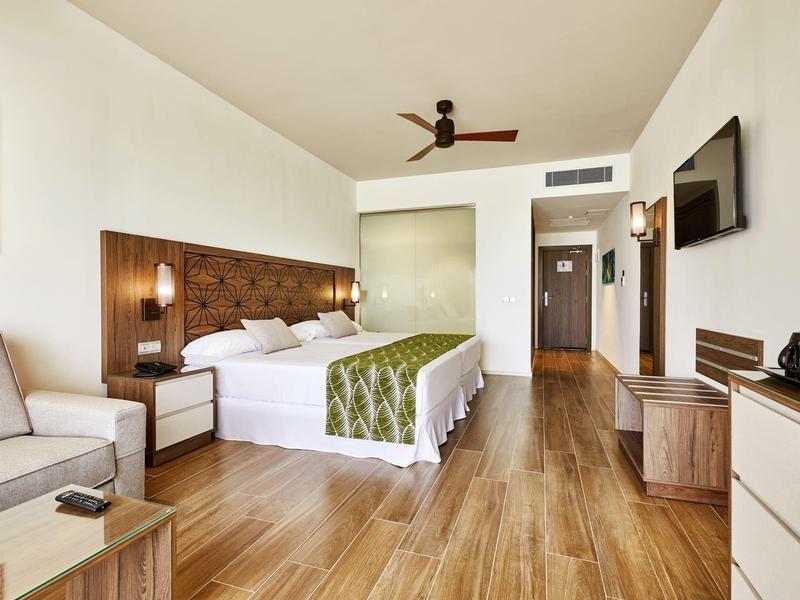 Modernes Hotelzimmer mit großem Bett, Sofa, Holzboden und TV an der Wand.