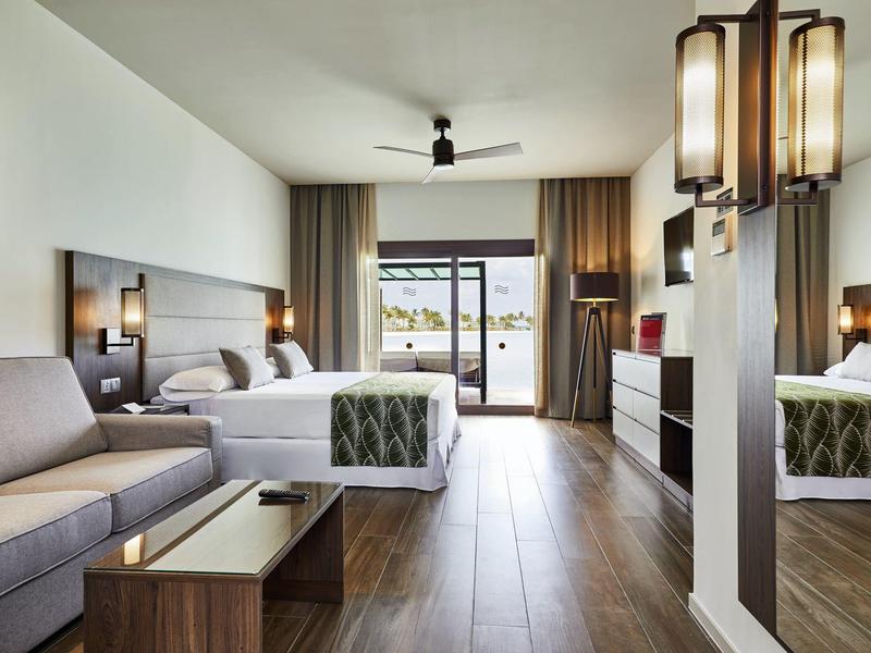 Modernes Hotelzimmer mit Doppelbett, Sofa, Holzboden und Blick auf Balkon.