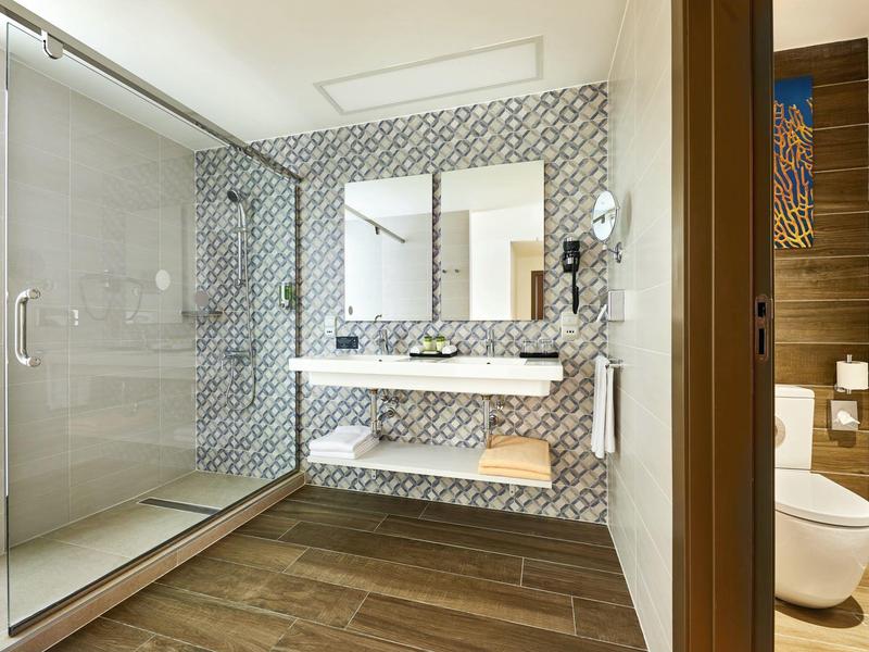 Modernes Badezimmer mit Holzfußboden, Glasscheibendusche und zwei Waschbecken an einer gemusterten Wand.