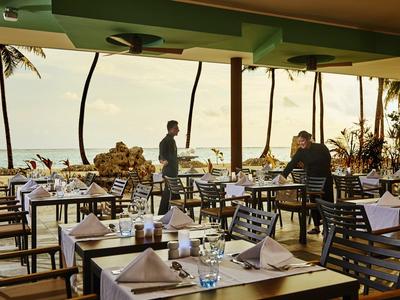 Restauracja na świeżym powietrzu z widokiem na morze i palmy o zmierzchu.