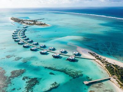 Überwasserbungalows vor einer Insel mit klarem türkisfarbenem Wasser und weißem Sandstrand.