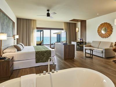 Geräumiges Hotelzimmer mit Meerblick, Doppelbett, Sofa, Badewanne und moderner Einrichtung.