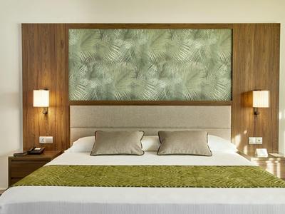 Modernes Hotelzimmer mit großem Bett, grüner Tagesdecke und dekorativem Wandbild.