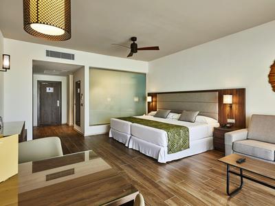 Modernes Hotelzimmer mit zwei Betten, Sitzecke, Holzboden und gedämpfter Beleuchtung.