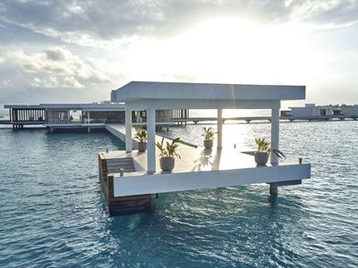 Offene Lounge auf einem Steg über klarem Meerwasser mit Blick auf den Horizont.