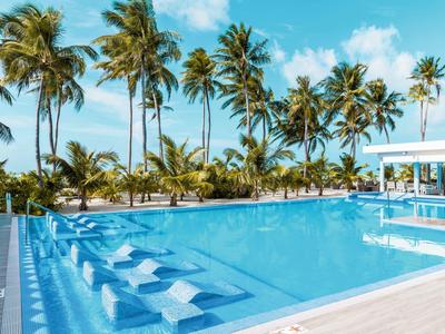 Moderner Pool mit Liegestühlen im Wasser, umgeben von Palmen und klarem Himmel.