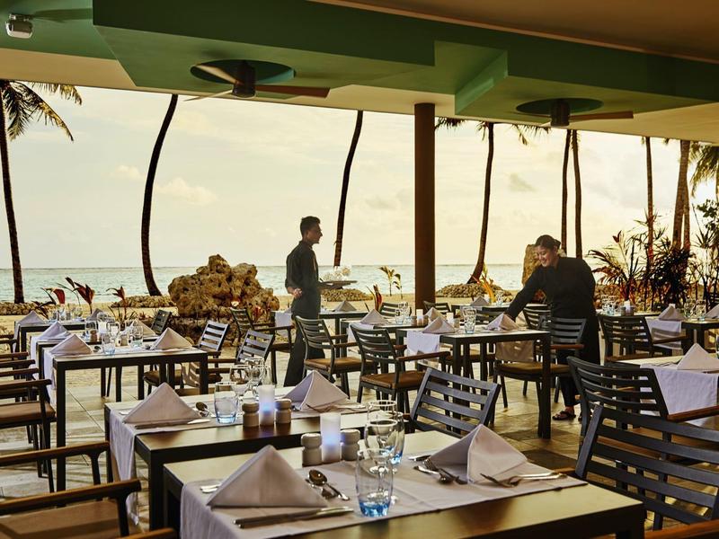 Restaurantterrasse mit gedeckten Tischen und Meerblick bei Sonnenuntergang.