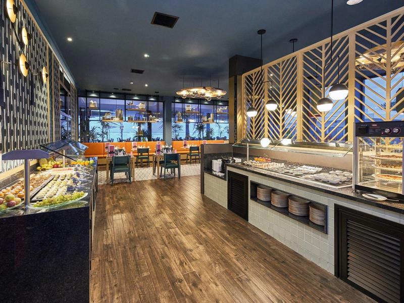 Modernes Restaurant mit Buffetbereich, hölzernem Boden und Sitzbereichen am Fenster.