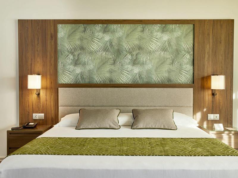 Modernes Doppelbett mit Holzrahmen, grüner Bettdecke und Blattmuster an der Wand