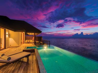 Luxuriöser Pool mit Holzboden und Sonnenliegen bei Sonnenuntergang über dem Meer.