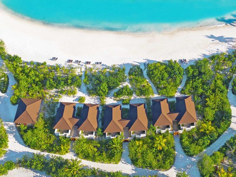 Vogelperspektive auf sechs Strandvillen mit braunen Dächern, weißen Sandstrand und türkisem Meer.