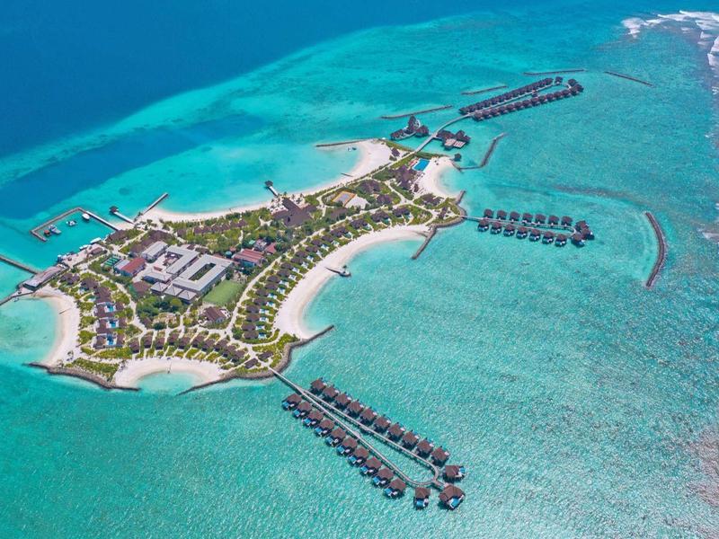 Tropische Insel mit Bungalows über klarem, türkisblauem Wasser und weißem Sandstrand.