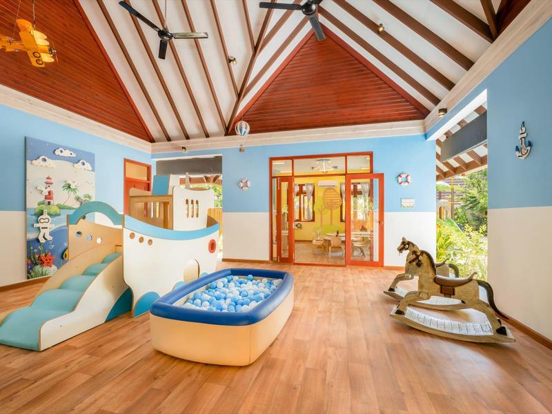 Heller, kinderfreundlicher Raum mit Holzfußboden, Rutsche, Bällebad und Schaukelpferden.