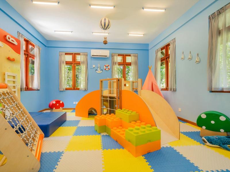 Helle Kinderspielecke mit buntem Schaumstoffboden, Klettergerüst und großen Fensterflächen.