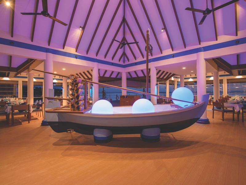 Großer Innenraum mit hölzernem Gestell, violetter Beleuchtung und einem Bootsmodell in der Mitte.