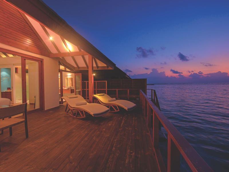 Terrasse mit Liegestühlen am Meer bei Sonnenuntergang, warmes Licht und ruhige Atmosphäre.