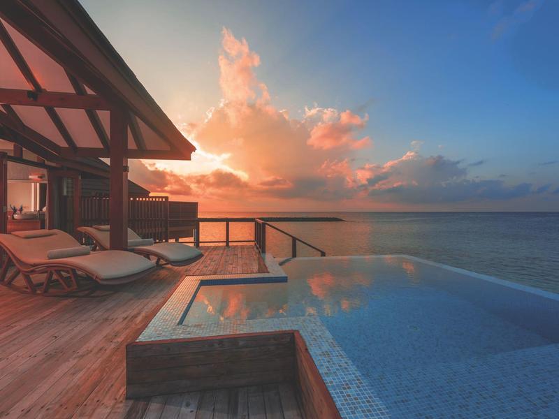 Luxuriöser Poolbereich mit Holzdeck und Liegestühlen bei Sonnenuntergang am Meer.