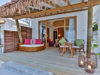 Gemütliche Terrasse mit Holzbohlen, rundem Sofa, bunten Kissen und kleinem Esstisch mit Stühlen.
