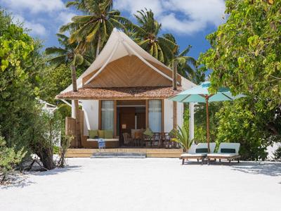 Bungalow am Strand mit weißen Liegen, Palmen und blauem Himmel im Hintergrund.
