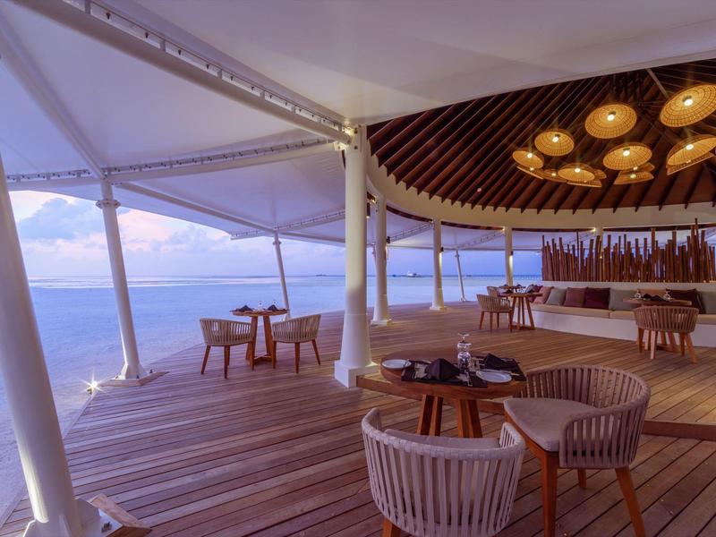 Moderner Außenbereich mit Holzterrasse, Korbstühlen und gemütlichem Barbereich bei Sonnenuntergang.