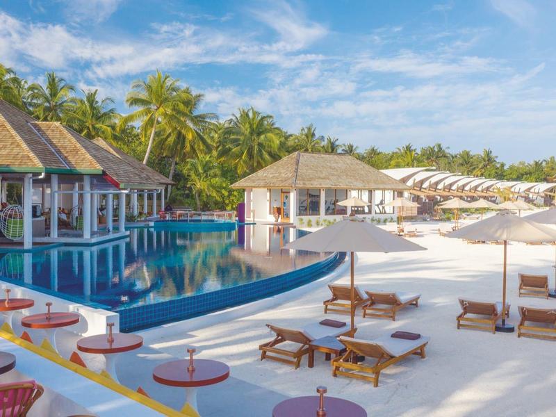 Luxuriöse Poolanlage mit Sonnenliegen, Palmen und blauem Himmel in tropischer Umgebung.