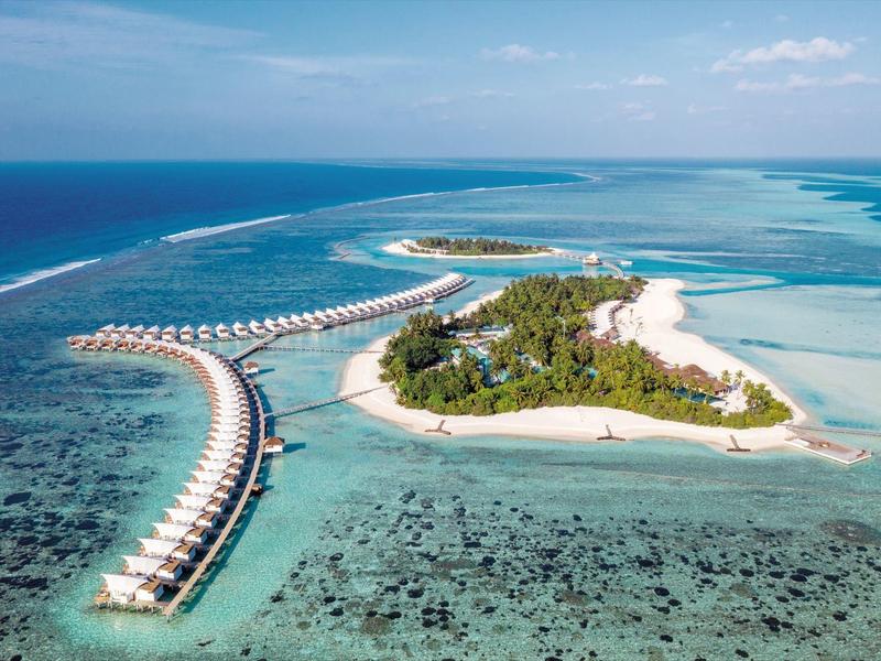 Tropische Insel mit weißen Sandstränden, Palmen und über Wasser gebauten Bungalows im klaren blauen Meer.