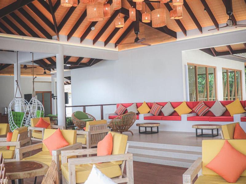 Hell gestalteter Wohnraum mit Holzbalken, roten und gelben Kissen und auffälliger Deckenleuchte.