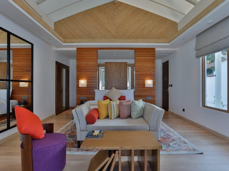 Modernes Wohnzimmer mit hoher Decke, bunten Kissen und großem Fenster, helle Holzböden und Wände.