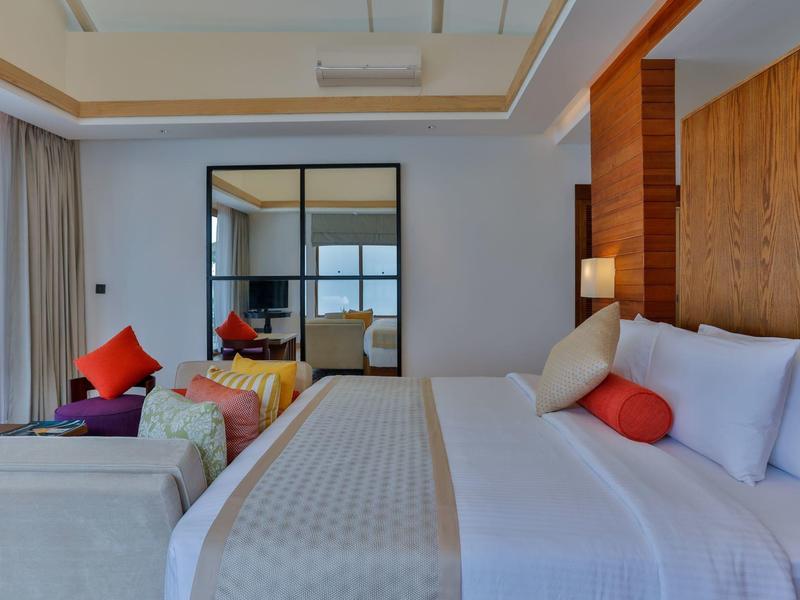 Helles Schlafzimmer mit großem Bett, bunten Kissen, Sofa und großem Spiegel an der Wand.