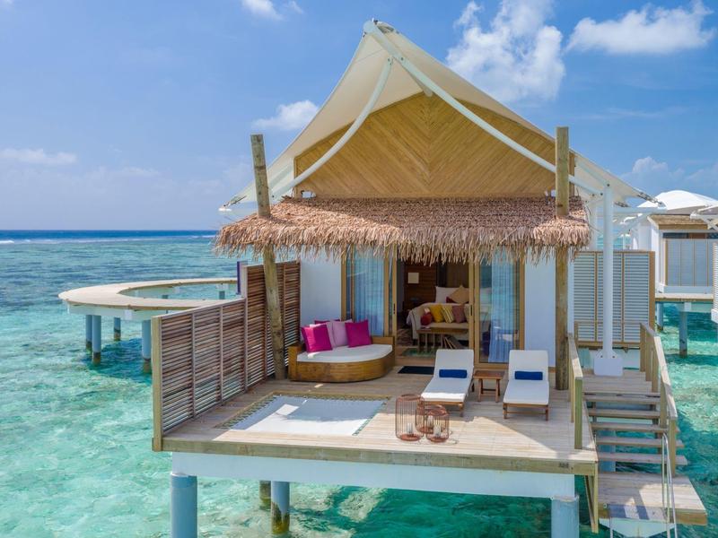 Bungalow auf Stelzen über klarem türkisfarbenem Wasser mit Sonnenschirm und gemütlicher Terrasse.