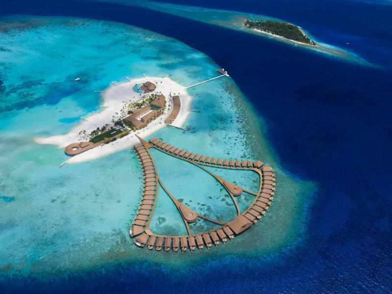 Insel mit Sandstrand, umgeben von türkisblauem Wasser und schwimmenden Bungalows.