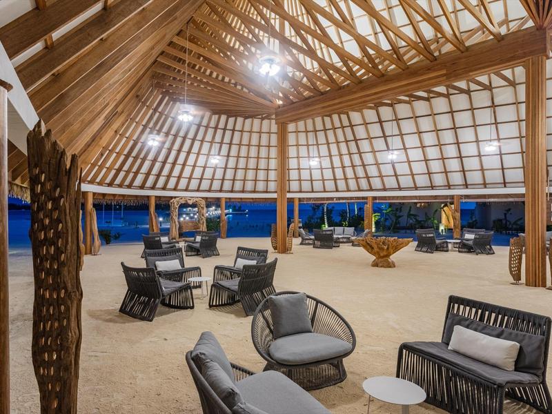 Offener Pavillon mit Holzstützen, möbliert mit schwarzen Sesseln und kleinen weißen Tischen.