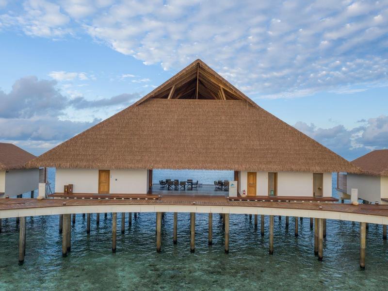 Ein Haus aus Holz und Stroh steht auf Pfählen im klaren Meerwasser unter blauem Himmel.