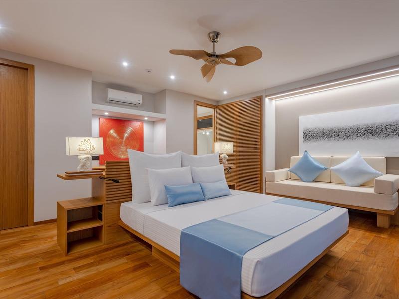 Modern eingerichtetes Hotelzimmer mit Doppelbett, Holzboden und Sitzbereich mit Sofa und Kissen.