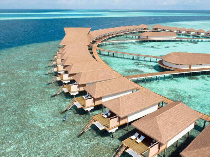 Überwasserbungalows mit braunen Dächern, die sich über klares, türkisfarbenes Wasser erstrecken.