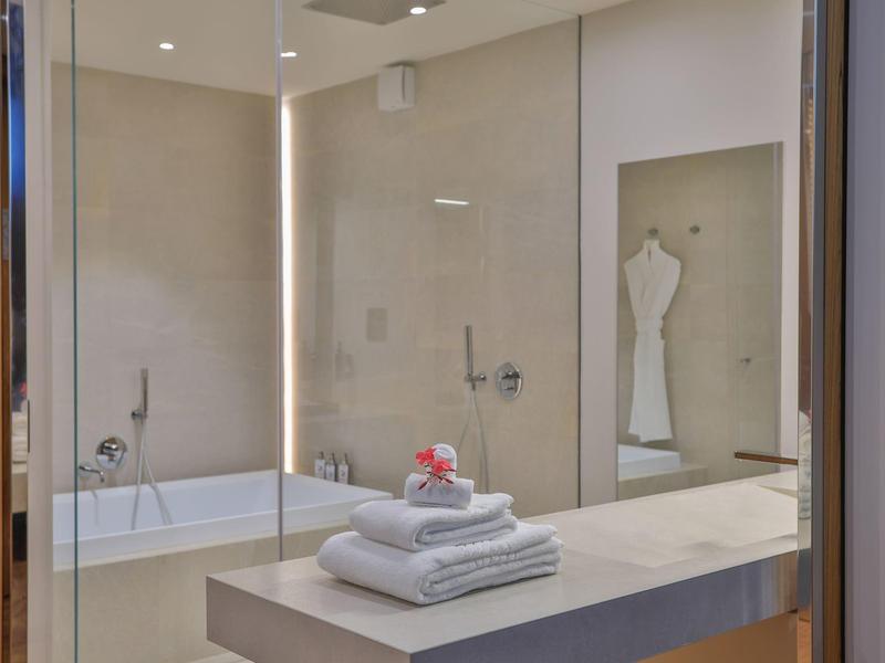 Modernes, helles Badezimmer mit Badewanne, großem Spiegel und weißem Handtuchstapel auf Theke.