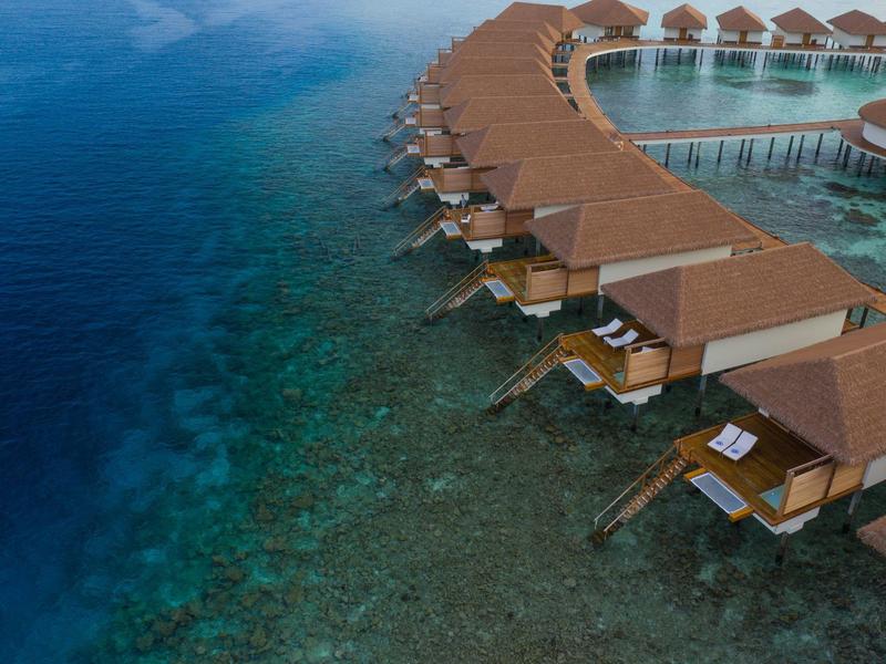Reihen von Wasserbungalows mit Strohdächern über klarem, türkisfarbenem Meerwasser.