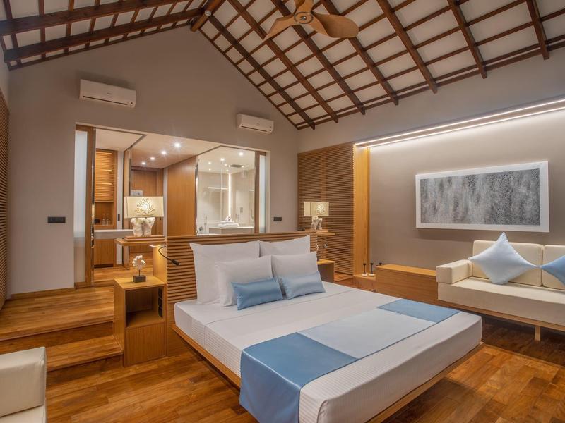 Moderner, offener Schlafzimmerbereich mit Holzdecke, Doppelbett, Sofa und Badezimmer im Hintergrund.