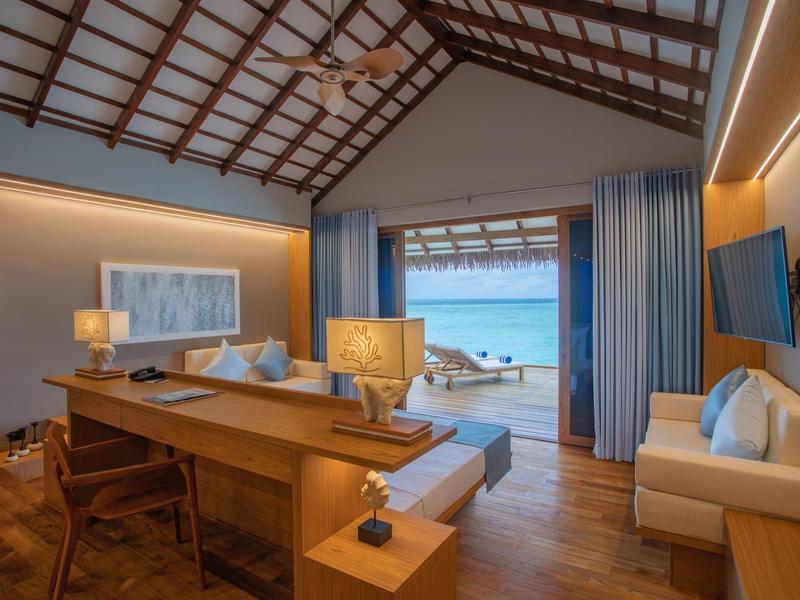 Helles Wohnzimmer mit Holzboden, Deckenbalken, modernen Möbeln und Blick auf Strand und Meer.