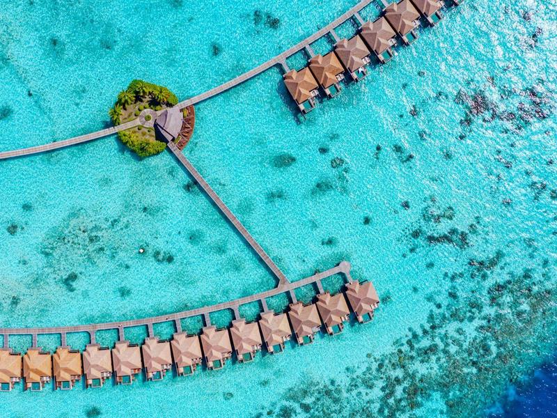Luftaufnahme von Überwasserbungalows in einem türkisfarbenen Ozean mit zwei Stegen.