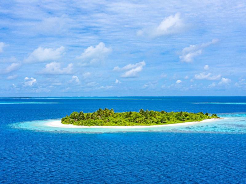 Kleine tropische Insel mit üppiger Vegetation umgeben von klarem, blauem Wasser unter einem bewölkten Himmel