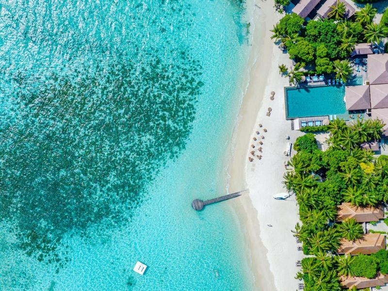 Luftaufnahme eines Resorts mit weißem Sandstrand, klarem blauem Wasser und Liegestühlen am Pool.